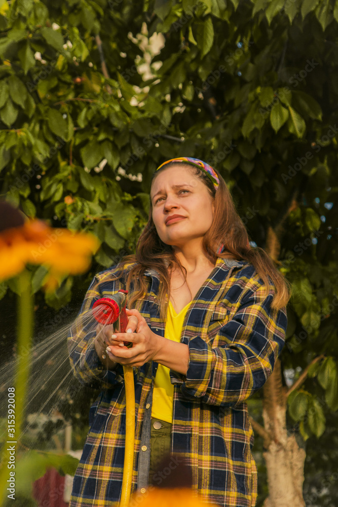 young pretty girl having fun in the garden watering plants with a hose. Smiling while taking a favorite hobby. young pretty girl having fun in the garden watering plants with a hose. Smiling while taking a favorite hobby.