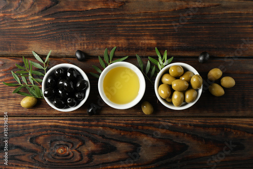 Bowls with olives and oil on wooden background, space for text