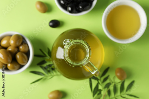 Olives, bottle and bowl with olive oil on green background, top view and close up