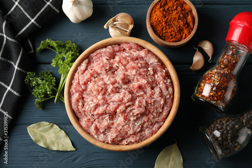 Spices and bowl with minced meat on wooden background, top view