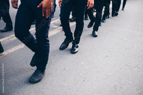 Low section of men in black trousers marching on concrete path. Selected focus. Copy space. 