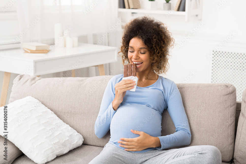 Relaxed future mom eating chocolate bar, resting on sofa Relaxed future mom eating chocolate bar, resting on sofa