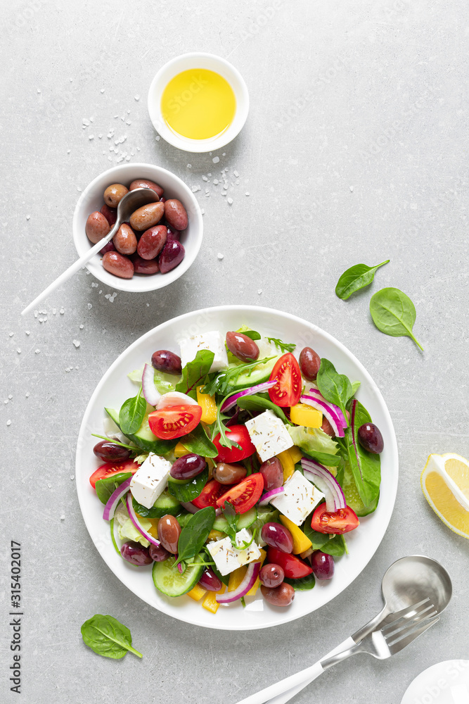 Greek salad with greens, olives and feta chesse on a white plate, top view Greek salad with greens, olives and feta chesse on a white plate, top view