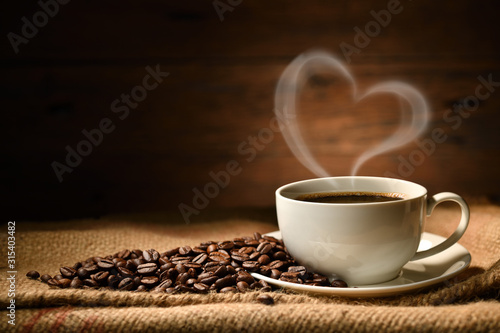 Filiżanka kawy z kierowym kształta dymem i kawowymi fasolami na burlap worku na starym drewnianym tle