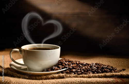 Cup of coffee with heart shape smoke and coffee beans on burlap sack on old wooden background
