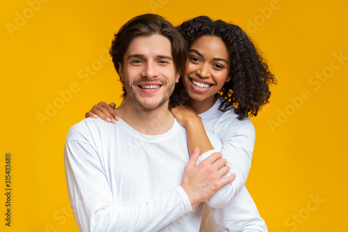 Romantic interracial couple embracing and posing over yellow background photo