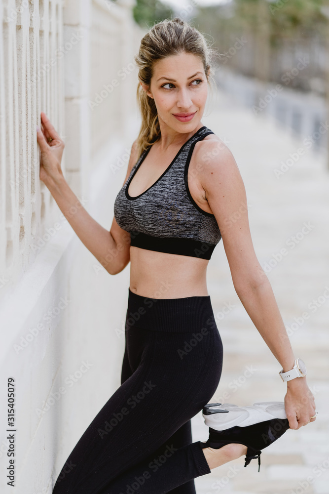 Side view of motivated sporty woman in active wear standing on one leg while holding another foot with hand and looking away Side view of motivated sporty woman in active wear standing on one leg while holding another foot with hand and looking away