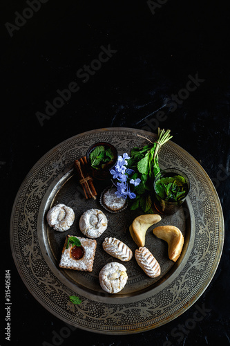 Traditional tea with mint and assorted homedade Arab sweets on dark background. Ramadan. Islamic. Halal photo