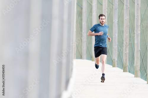 Highly motivated bearded male athlete in blue t shirt and shorts running outdoors under cover looking at camera photo