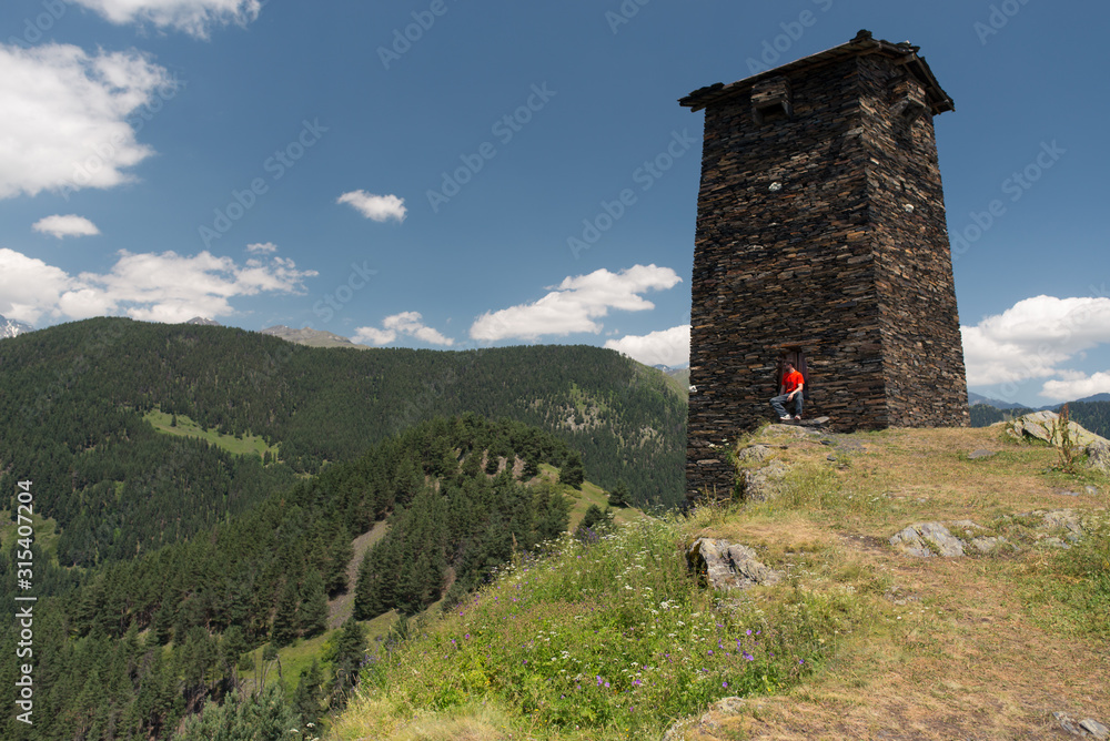 Man sitting in a solitary ancient tower with stone walls at outskirts of village against amazing view of green forested hills and misty valley in Georgia Man sitting in a solitary ancient tower with stone walls at outskirts of village against amazing view of green forested hills and misty valley in Georgia
