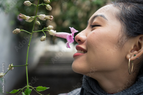 Closeup of crop Asian female on vacation smiling while enjoying smell of purple flower with lane on blurred background at Albaicin in Granada