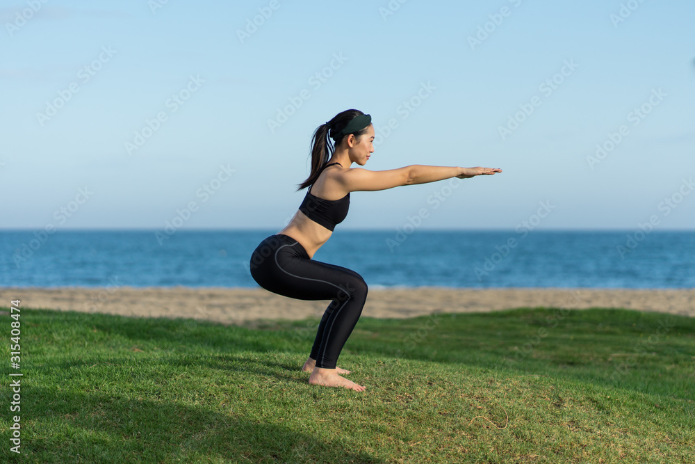Young slim female in black top and leggings standing on green grass practicing yoga on beach Young slim female in black top and leggings standing on green grass practicing yoga on beach