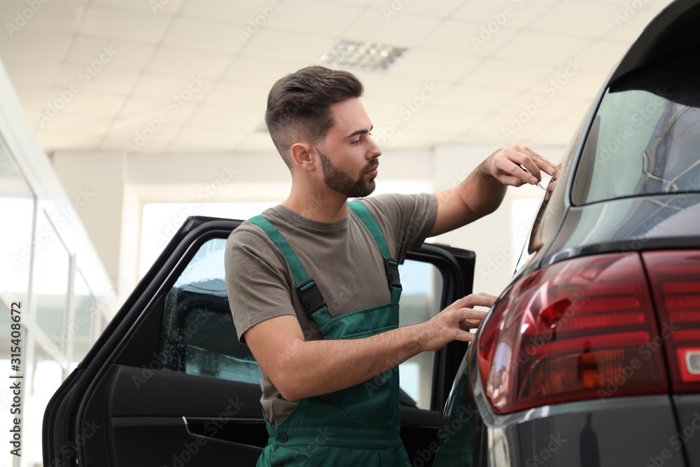 Worker tinting car window with foil in workshop Worker tinting car window with foil in workshop