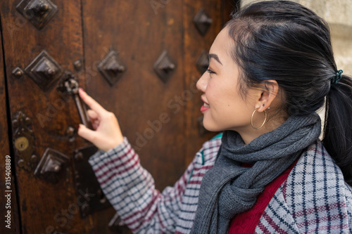 Curious female traveler in casual wear clattering in ancient door at city street photo