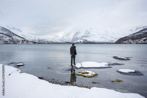 Unrecognizable male in warm clothes looking away and enjoying amazing wintry scenery of highland while standing on shore of Kaldfjorden lake in Norway photo