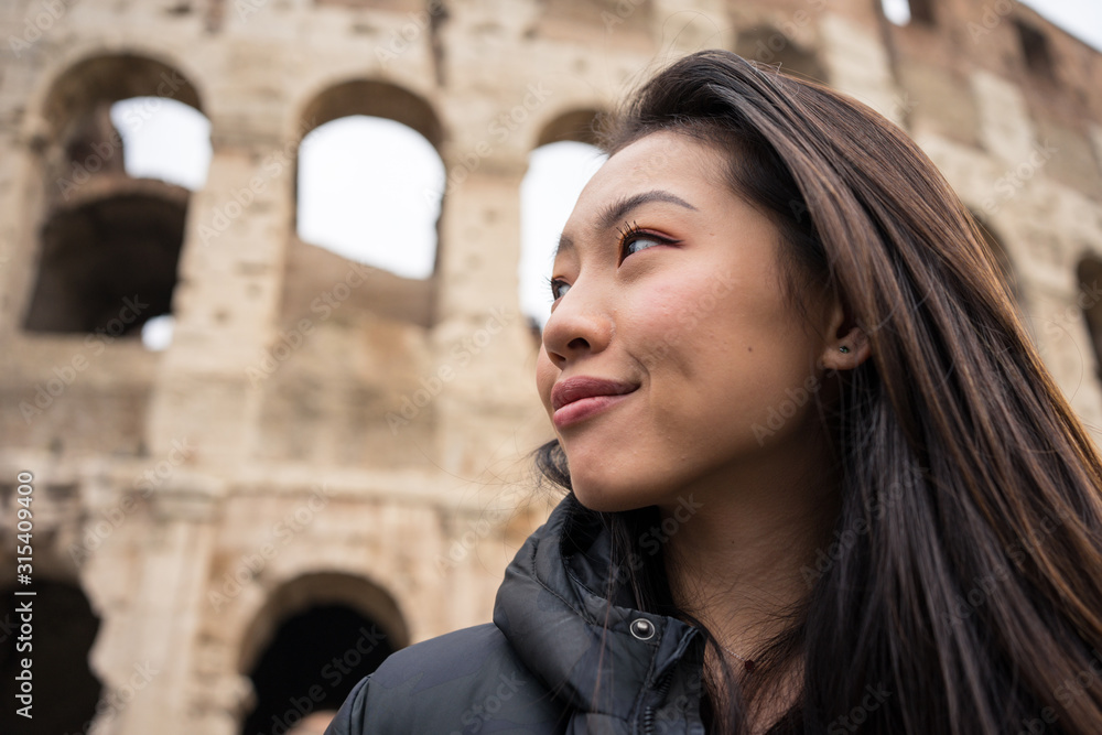 From bellow happy ethnic woman smiling and looking away while standing on blurred background of Colosseum on street of Rome, Italy From bellow happy ethnic woman smiling and looking away while standing on blurred background of Colosseum on street of Rome, Italy