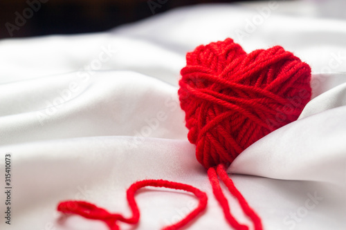 white silk fabric with bends and a red knitted heart with nicknames for Valentine's Day, copy space .close up