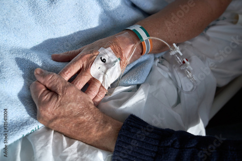 From above mature male holding hand of ill female on bed while visiting patient in hospital ward photo