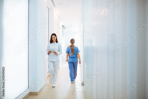 Cheerful doctor in white uniform reading document while walking along light corridor in clinic photo