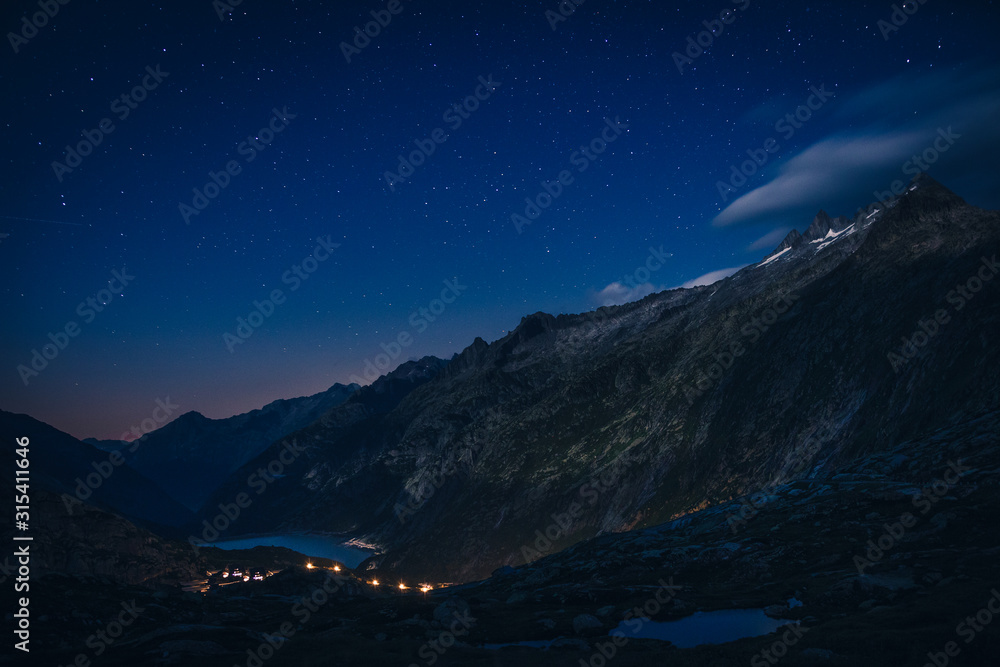 Mountain range and river between slopes with burning lights above in Switzerland Mountain range and river between slopes with burning lights above in Switzerland