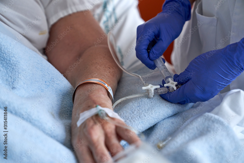 Crop nurse injecting medication into mature patient arm Crop nurse injecting medication into mature patient arm
