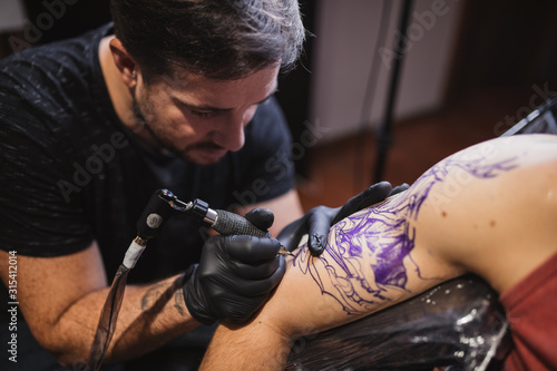 Master doing tattoo on forearm of male customer photo