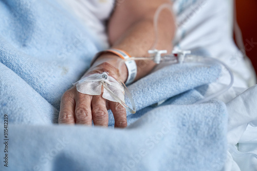 Unrecognizable mature person with cannula with remedy attached to arm lying on medical med during recovery in hospital photo