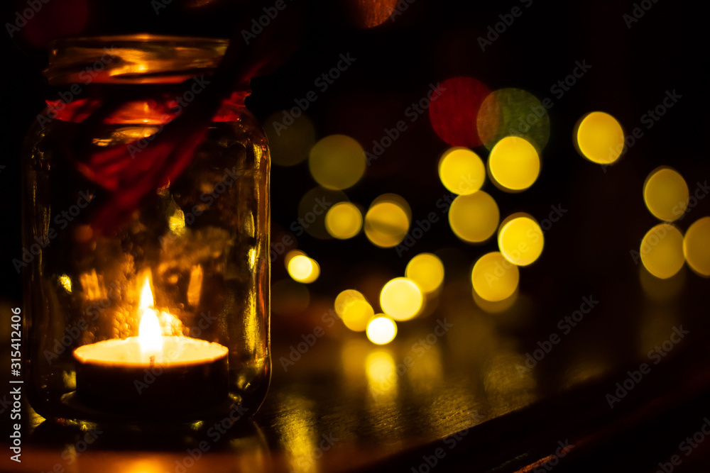 A small candle burns in a jar in the dark against the background of bokeh lights A small candle burns in a jar in the dark against the background of bokeh lights