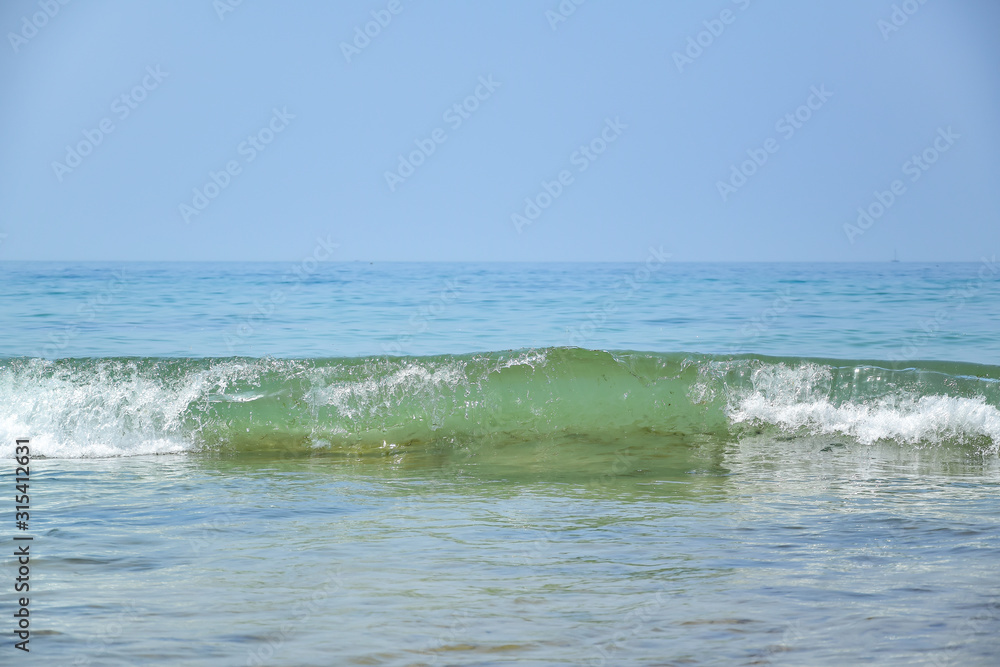 Portimao / Algarve, Portugal - A small wave with white foam goes to the shore, blue ocean, blue sky, in the summer afternoon.