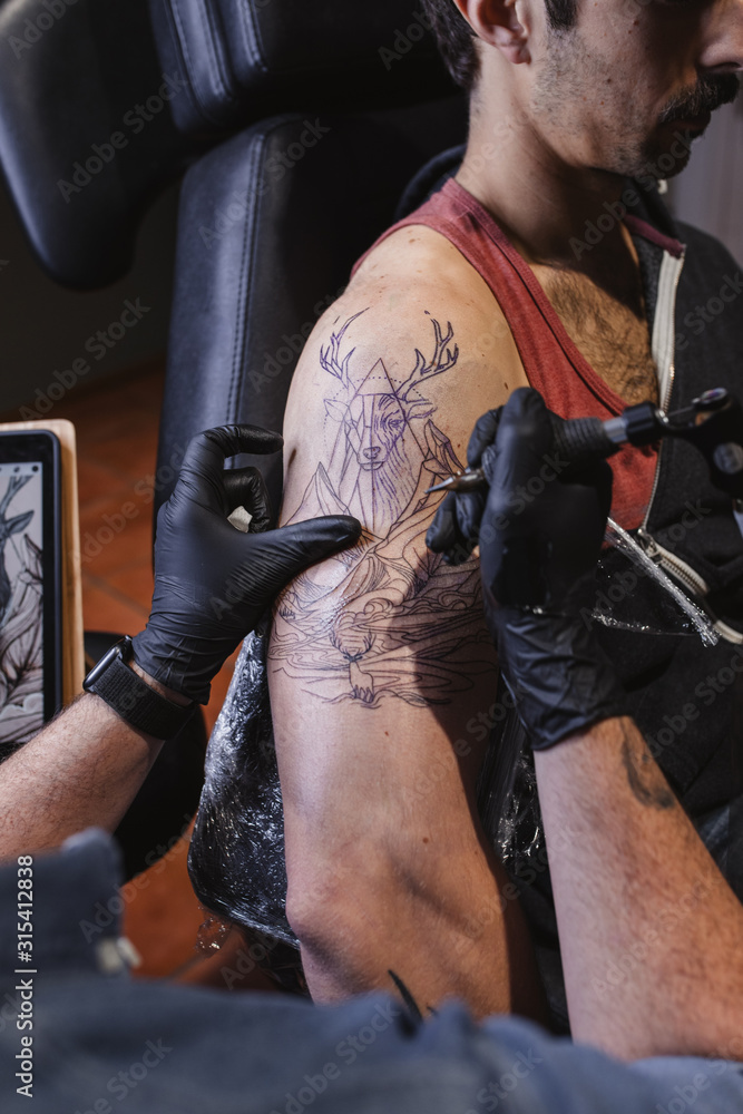 Master doing tattoo on forearm of male customer Master doing tattoo on forearm of male customer