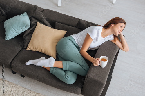 Εκτύπωση καμβά overhead view of attractive woman chilling of sofa with cup of tea