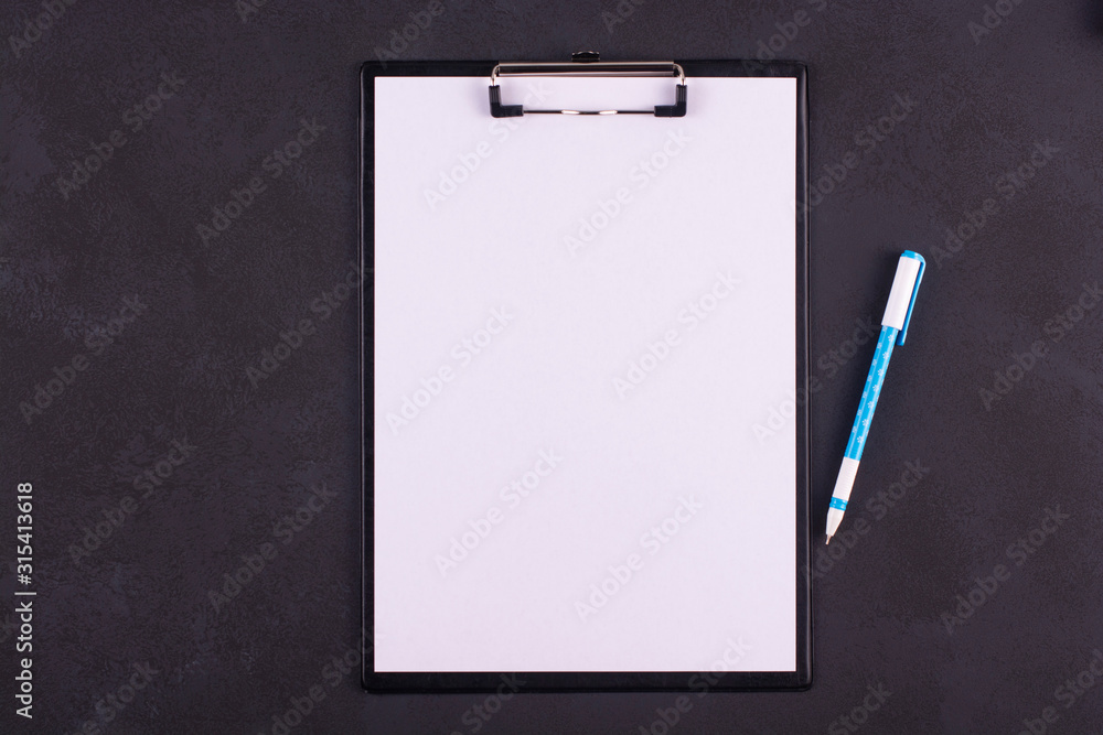 Clipboard with white blank paper and pen on a black table. Clipboard with white blank paper and pen on a black table.
