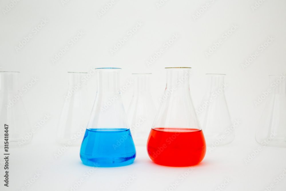 Scientific laboratory glass erlenmeyer flask filled with blue and red liquid with glassware equipment on white background. Scientific laboratory glass erlenmeyer flask filled with blue and red liquid with glassware equipment on white background.