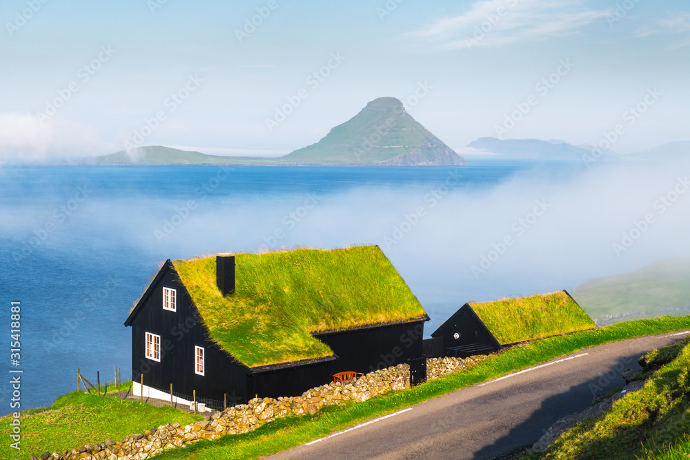 Foggy morning view of a house with typical turf-top grass roof in the Velbastadur village on Streymoy island, Faroe islands, Denmark. Landscape photography