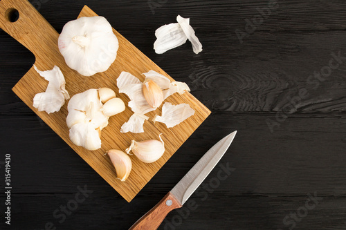 Dry garlic on the brown cutting board on the black wooden background. Top view. Copy space.