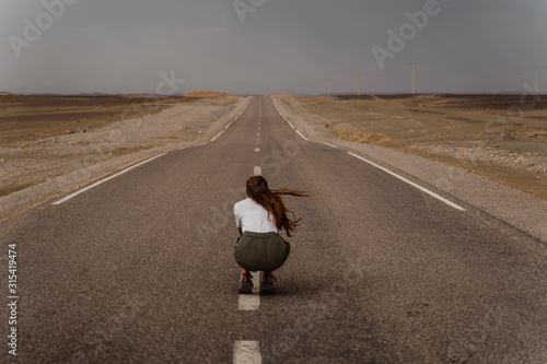 Back view of woman crouching on median strip of empty country road, Fez, Morocco photo