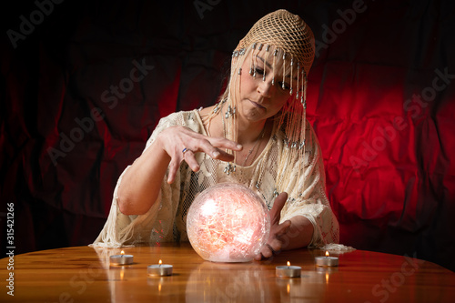 Φωτογραφία Fortune Teller with Crystal Ball on table with candles and black and red mottled