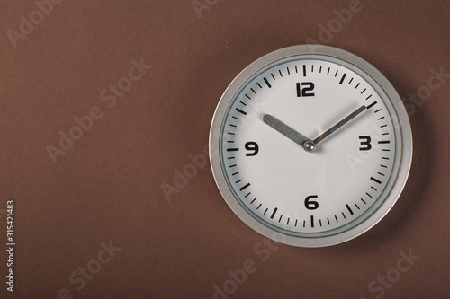 White wall clock with a yellow used hanging on the wall. Minimalist image of a wall clock on a brown background with copy space