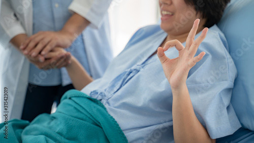 Medicine health care and trust concept.Doctor holds the hand of a patient as a sign of care and consolation.Young asian beautiful woman patient is smiling and raise up hand with OK sign symbol.