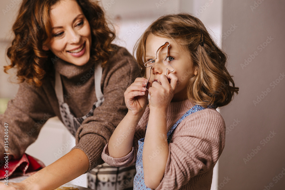 Playful girl with her mother holding Christmas cookie cutter in kitchen Playful girl with her mother holding Christmas cookie cutter in kitchen