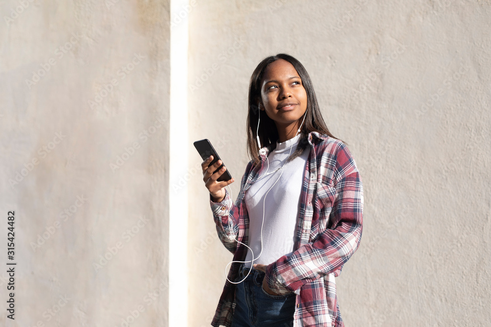 Fototapeta premium Portrait of African American young beautiful woman standing on the street while using a mobile phone