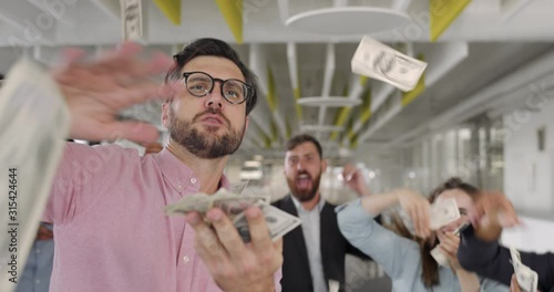 Excited businessman with team of mixed ethnic workers celebrating successful contract. Close up of office workers being happy, scattering and throwing money in modern office room.