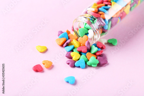 Colorful heart shaped sprinkles with glass bottle on pink background