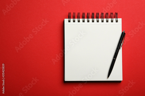 Stylish open notebook and pen on red background, top view. Space for text