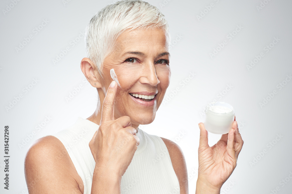 Gorgeous smiling Caucasian senior woman trying out new anti age cream. Beauty photography. Gorgeous smiling Caucasian senior woman trying out new anti age cream. Beauty photography.