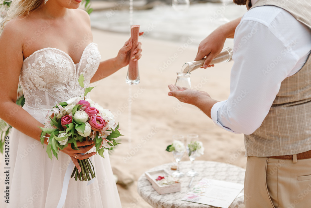 sand ceremony being performed at wedding, focus on bridal bouquet. hands of bride and groom doing sand ceremony during wedding sand ceremony being performed at wedding, focus on bridal bouquet. hands of bride and groom doing sand ceremony during wedding