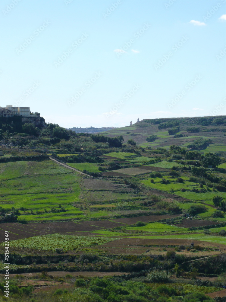 Gozo green valley with terracing, hilltop housing, skyline  church tower cleaving blue sky