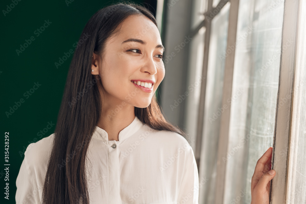Freestyle. Young woman standing looking out the window smiling cheerful Freestyle. Young woman standing looking out the window smiling cheerful