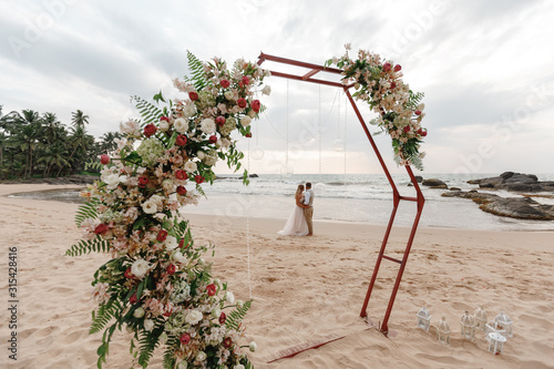 Bride and groom enjoying beach wedding in tropics, wedding arch, ocean background