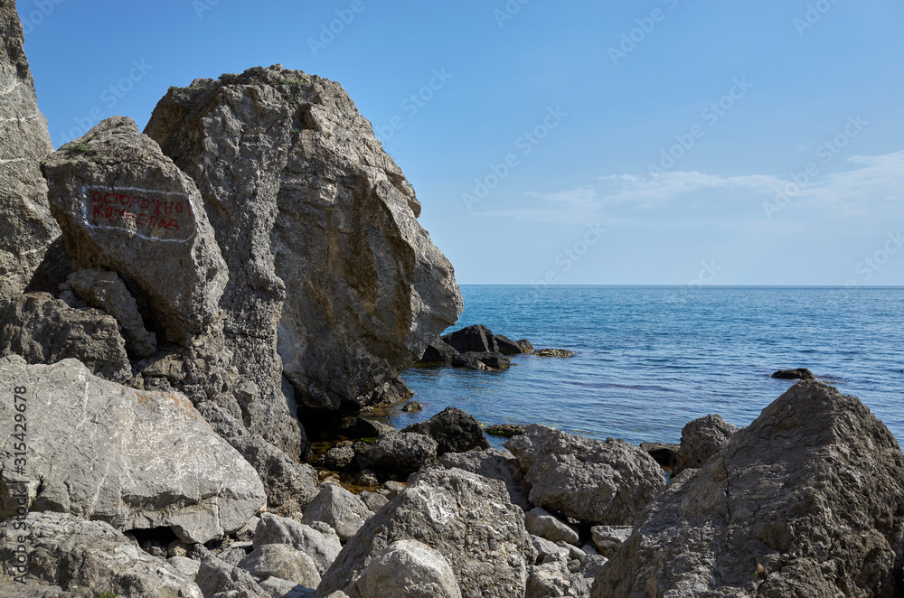 The rocky coast of the Black Sea. Cape Alchak in Sudak, Crimea. The inscription on the rock
